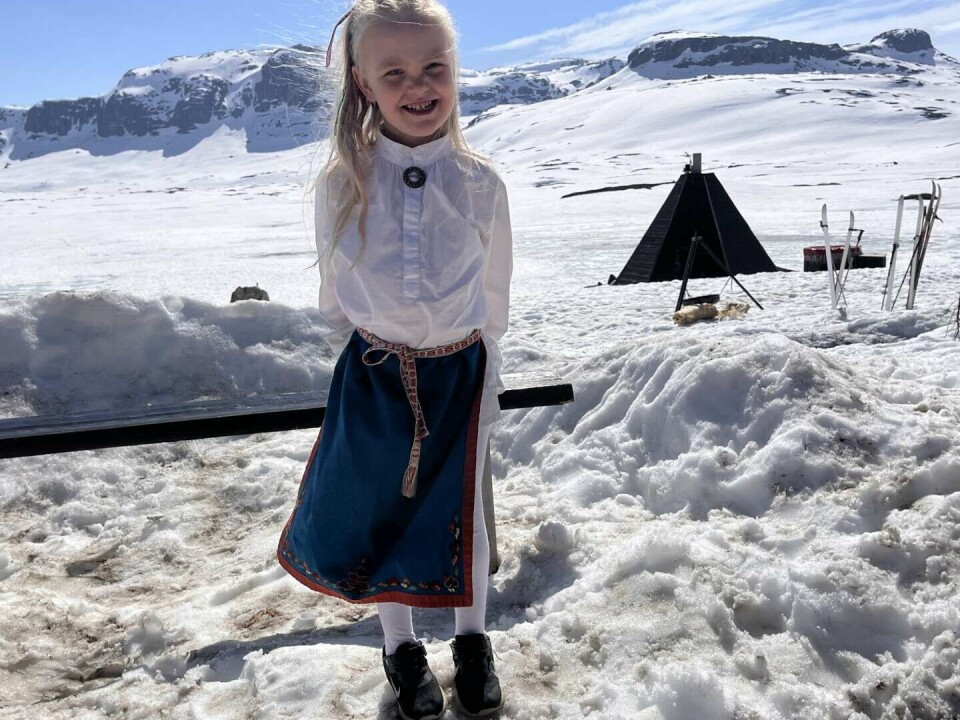 Signe Vesaas (4) har feira nasjonaldagen på Vinjar, men no har familien teke turen til Haukeliseter. Som mange andre, blei Signe litt forfylgd av bunaden, som ho har vrengt av seg. Men skjorte og fyrkle fungerer fint i godvêret 987 meter over havet. Kistenuten i bakgrunnen.