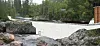 Betongdam over elv mellom steinar og skog.