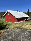 Raudt naust med kvitt tak i ei lysning ved skogen.