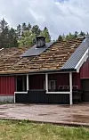 Raudt hus med delvis avdekka tak og skog i bakgrunnen.