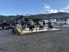 Folk står på ei treplattform i eit grustun ved bygningar og fjell.