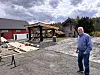 Mann på gruslagt tun ved hytte med treplatting og byggjematerialar.