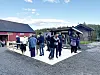 Folk står samla på ein uteplass ved eit raudt bygg.