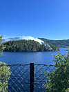 Skogkledd øy med røyk i ein innsjø, sett gjennom gjerde.