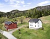 Raudt uthus og kvitt hus ved ein grusveg i grønt landskap.