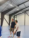 To menn med innebandykøller står på ein innandørs bane i ein idrettshall.