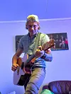 Person spelar akustisk gitar i eit rom med blått lys.