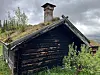 Svartna tømmerhus med torvtak i grønt landskap.