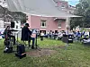 Musikar spelar på liten scene i park med publikum ved bord i bakgrunnen.