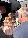 Ung kvinne i rosa kjole ser på mobilen framfor ein scene utandørs.