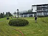 Brannfolk på grasbakke ved moderne bygning i regn og tåke.
