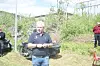 Ein mann står ved ei velta bil i eit uteområde med gras og buskar.