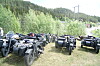 Fleire ATV-ar står på ei grasmark ved skog og fjell.