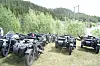 Fleire ATV-ar står på ei grasmark ved skog og fjell.