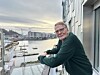 Mann står på ein balkong og ser utover ei hamn.