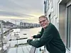 Mann står på ein balkong og ser utover ei hamn.