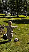 Barn med opne armar jaktar såpebobler på graset i ein park.