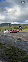 To motorsyklistar hoppar over bilar på ein asfaltplass.