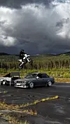 Motorsyklist hoppar over ein BMW på asfaltplass under mørke skyer.