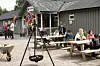 Folk sit ved piknikbord utanfor ein kafé med norske flagg.