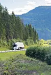 Lastebil køyrer på veg ved skog og fjell.