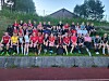 Stor gruppe posar på tribune med fotballbane framfor klubbhuset.