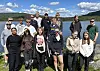 Ei gruppe på 15 personar står ved eit vatn under blå himmel.