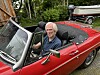 Ein mann sit i ein raud kabriolet på ein oppkøyrsel.