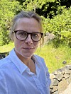 Kvinne med briller tek sjølvportrett utandørs i ein hage.