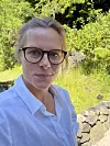 Kvinne med briller tek sjølvportrett utandørs i ein hage.