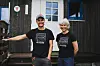 To personar står framfor eit svart trehus.