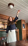 Kvinne med løfta arm i ein bar med treveggar.