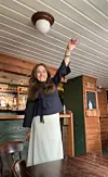 Kvinne med løfta arm i ein bar med treveggar.