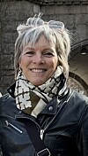 Ei kvinne smiler framfor ein steinboge utandørs.