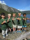 Fem barn står på ein steinmur ved ei innsjø og viser tommelen opp.