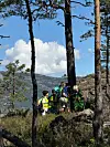 Gruppe turgåarar står på ein bergknaus i skog med utsikt over vatn og fjell.