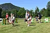 Folk står og går på ei grasbane med målrammer og fjell i bakgrunnen.