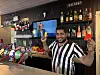 Bartender held opp to farga drikkevarer bak ein bar.