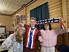 Tre personar står framfor norske flagg og teksten «NORGES» i eit rom med treveggar.