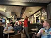 Gjestar sit i ein bar medan ein mann i raud genser står med armane i vêret.