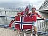 Tre personar held eit norsk flagg ved vatnet.
