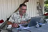 Mann ved bord med laptop, notatblokk og mobil utandørs.