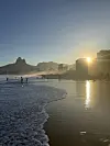 Sol over strand med bølgjer, folk og bygningar i bakgrunnen.