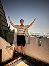 Mann står på takterrasse med armane opp, med bylys i bakgrunnen.