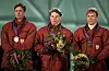 Tre norske kombinertutøvarar står på pallen med medaljar og blomsterbukettar.