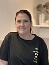 Kvinne i svart T-skjorte står framfor ei lys hyllevegg.