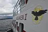 Kvitt skipsskrog med raud skrift og ørn-logo ved vatnet.