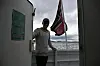 Person på båtdekk ved rekkverk og flagg i sterk vind.