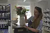 Kvinne held ein vase med blomster i ein butikk.