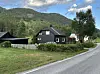 Svart hus ved veg i grønt bygdelandskap.